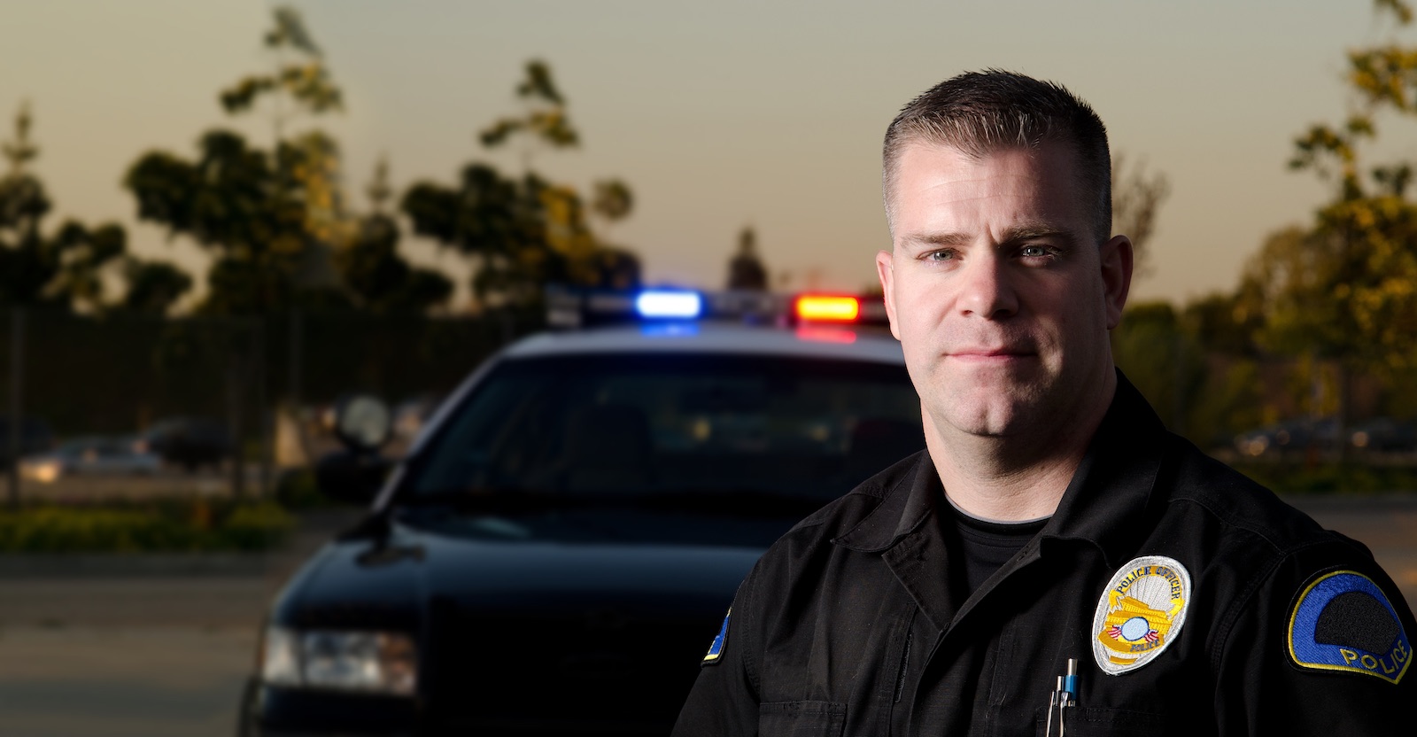 Male police officer by car looking at camera
