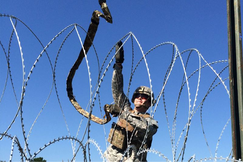 Soldier throwing a Bandolier across barbed wire